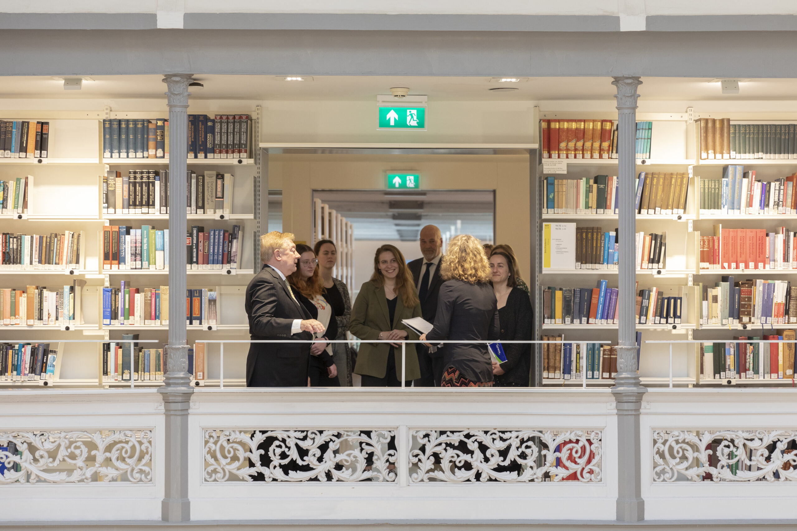 People standing on a balcony surrounded by bookshelves